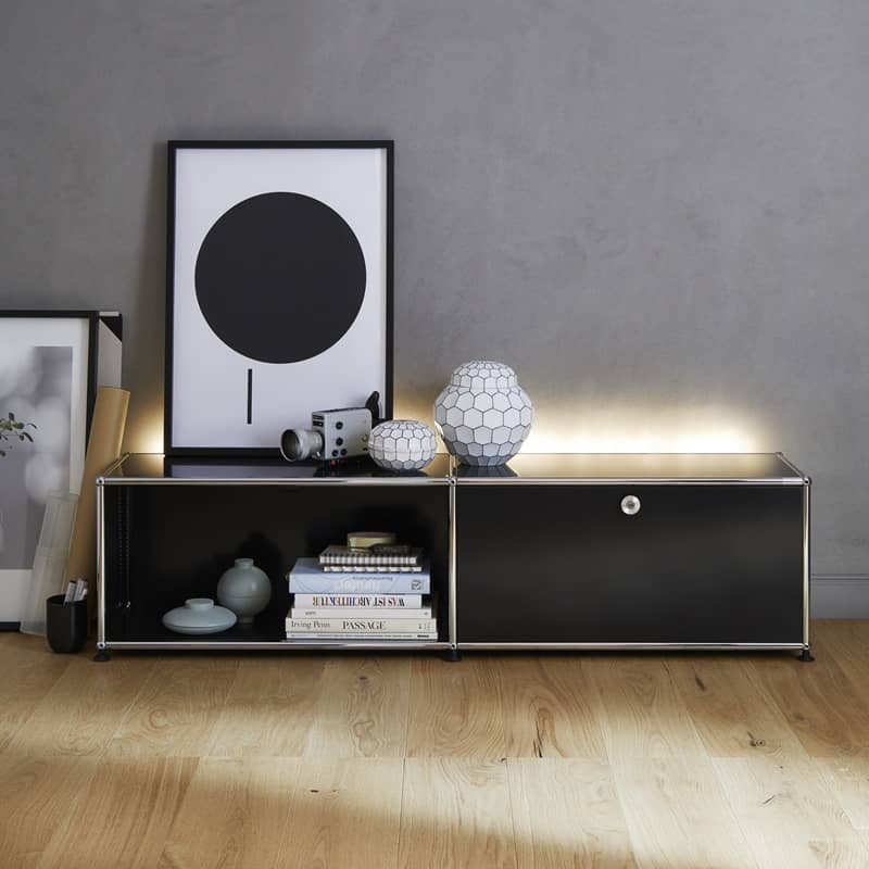 Ein schwarzes, mit Licht hinterleuchtetes Sideboard von USM Haller steht inklusive Accessores an einer Wand